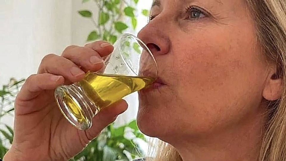 Nő otthon, kis pohárból issza az esti aranyszínű italt